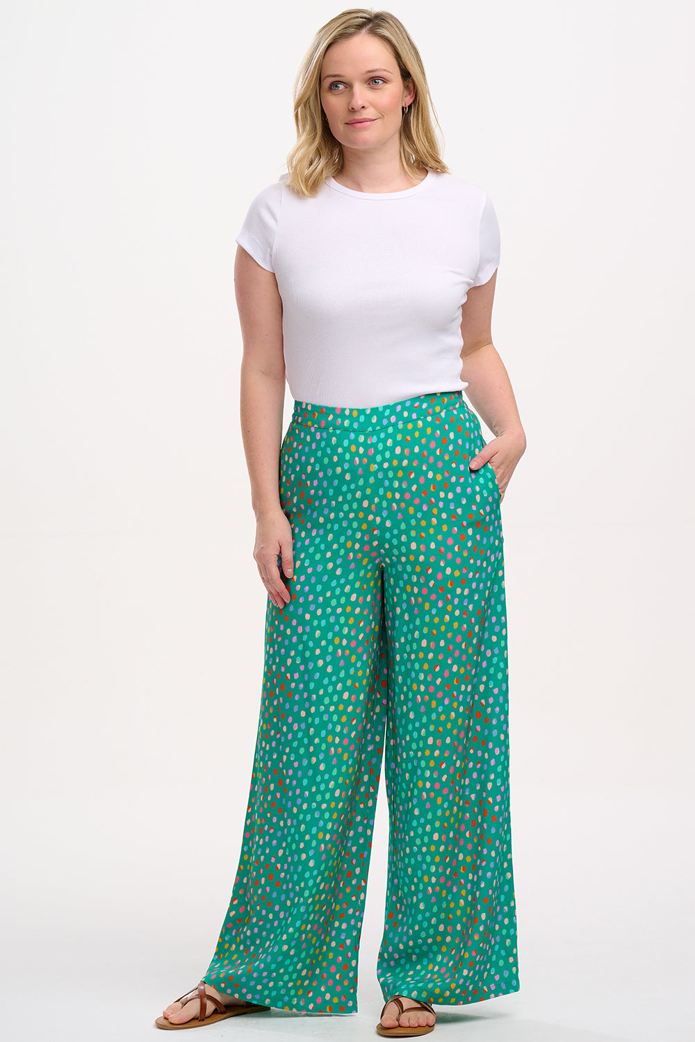 A woman modeling green palazzo pants with a multicolored dot pattern, paired with a white t-shirt.