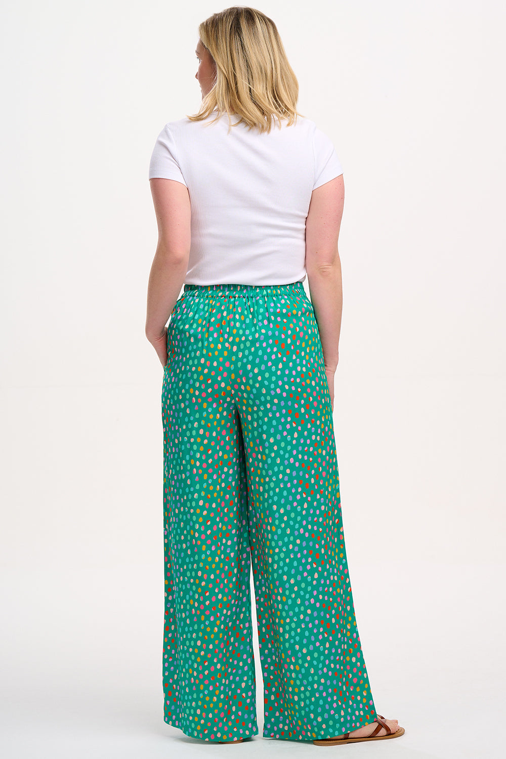 A woman modeling green palazzo pants with a multicolored dot pattern, paired with a white t-shirt.