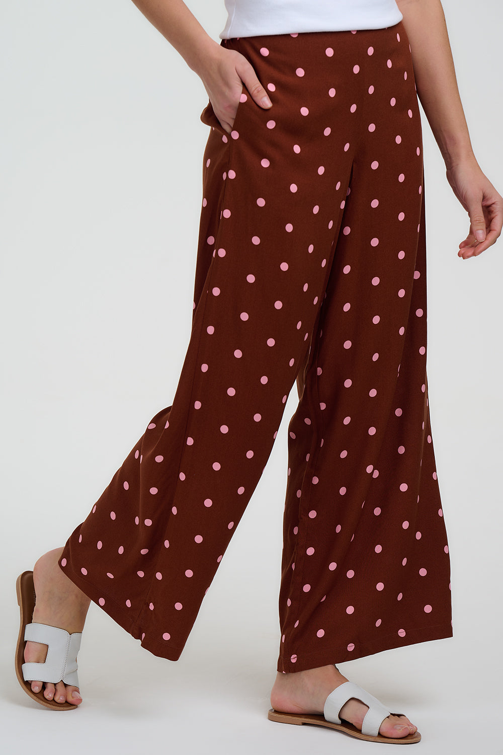 Brown wide-leg pants with pink polka dots worn by a person on a white background