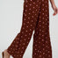 Brown wide-leg pants with pink polka dots worn by a person on a white background