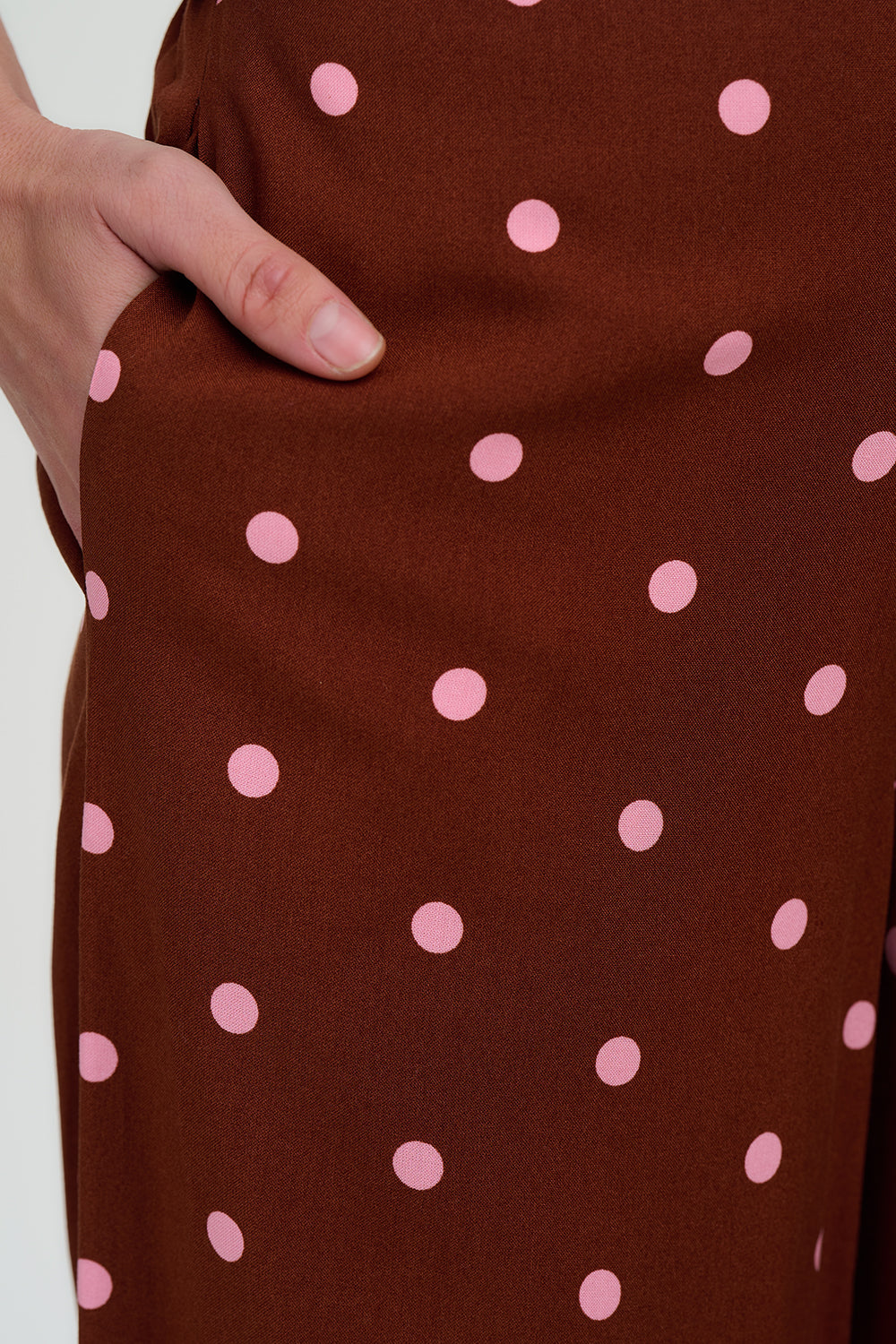 Brown fabric with pink polka dots and a hand touching it.