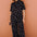Person wearing a black polka dot jumpsuit against a brown wall