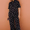 Person wearing a black polka dot jumpsuit against a brown wall