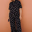 Person wearing a black polka dot jumpsuit against a brown wall