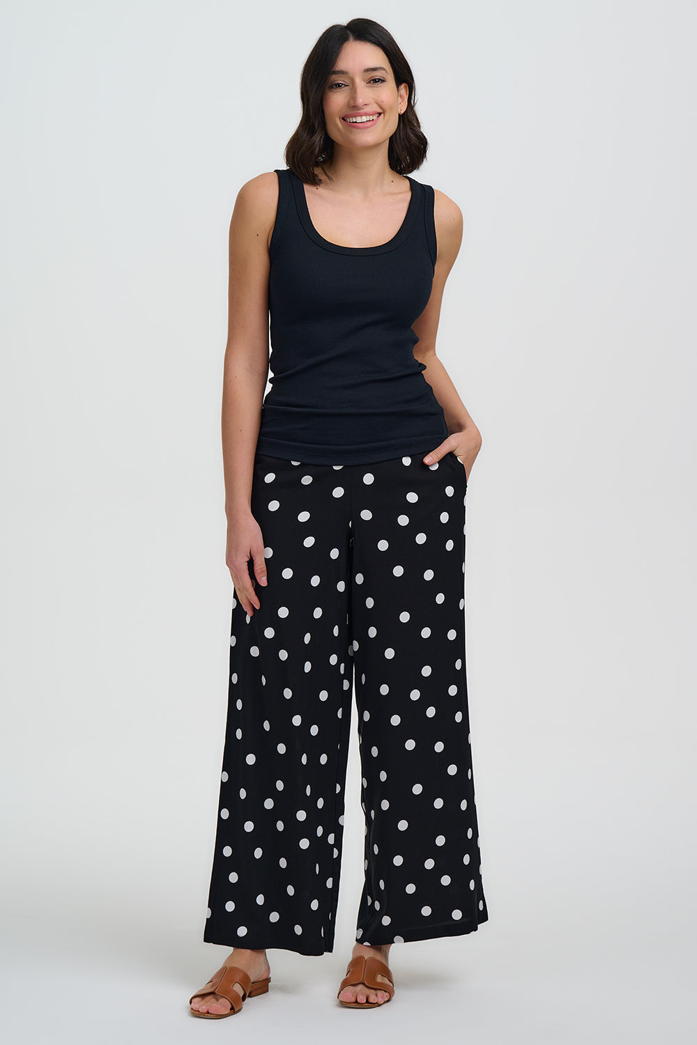 Woman wearing a black tank top and black pants with white polka dots on a white background