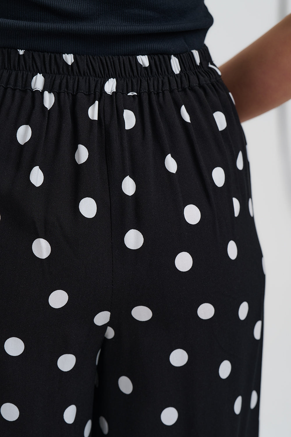 Black pants with white polka dots worn by a person against a white background