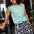 A person wearing a green sleeveless top with a floral folk print and black shorts with a similar floral pattern.