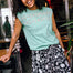 A person wearing a green sleeveless top with a floral folk print and black shorts with a similar floral pattern.