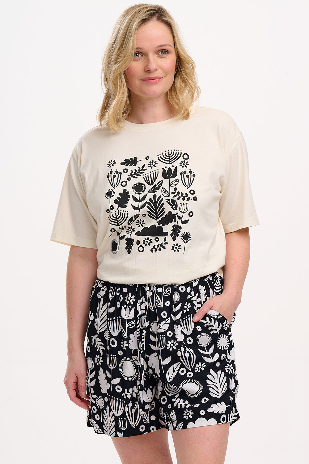 A person wearing a beige top with a black floral folk print and matching black and white patterned shorts with an elastic waistband and drawstring.