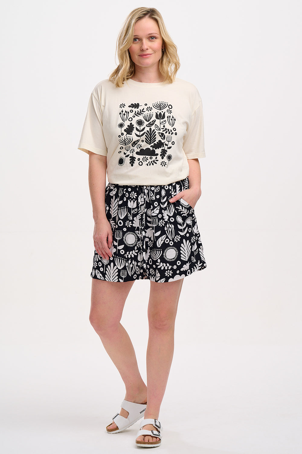 A person wearing a beige top with a black floral folk print and matching black and white patterned shorts with an elastic waistband and drawstring.
