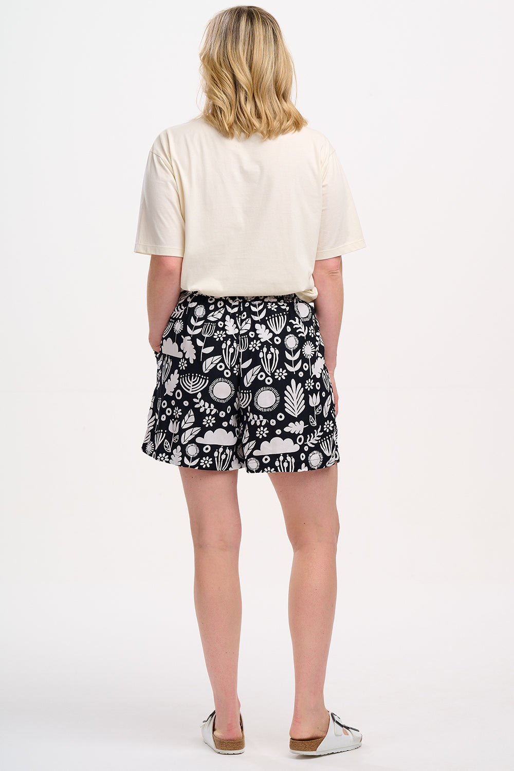 A person wearing a beige top with a black floral folk print and matching black and white patterned shorts with an elastic waistband and drawstring.