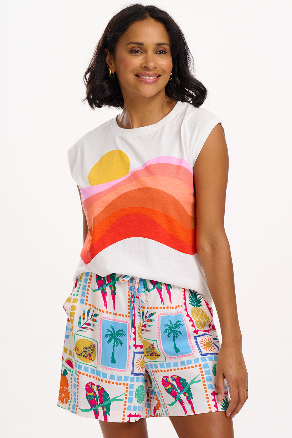 Woman wearing a colorful sleeveless top and patterned shorts on a white background