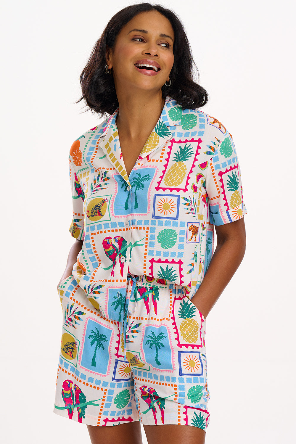 A woman standing, wearing off-white shorts with a multicolor jungle tile print, paired with a matching top, and brown sandals.