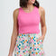 Woman wearing a pink tank top and colorful patterned shorts on a white background
