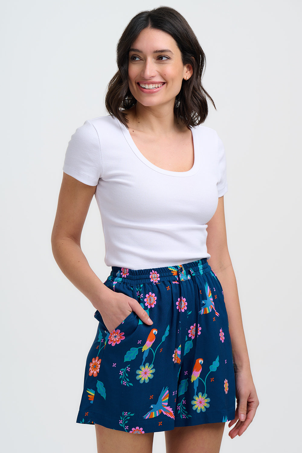 Woman wearing a white top and a navy blue skirt with colorful parrot pattern on a white background