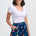 Woman wearing a white top and a navy blue skirt with colorful parrot pattern on a white background