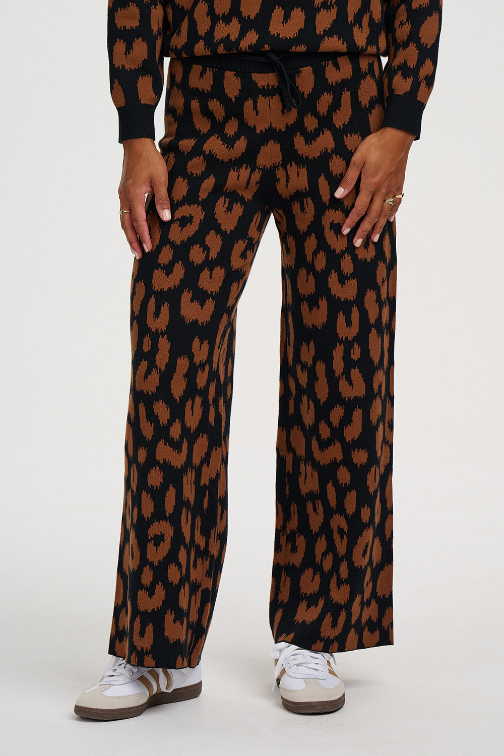 A person wearing a matching black and brown leopard-print outfit with wide-leg pants and white sneakers, shown from the waist down against a plain light background.