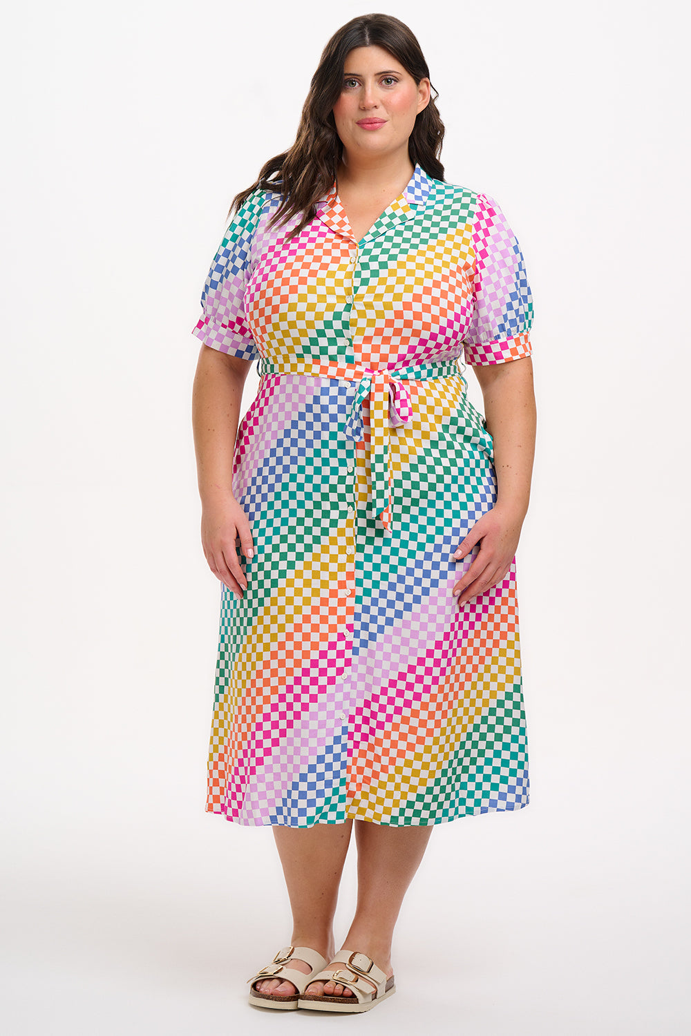 A model wearing a midi length shirt dress with a rainbow checkerboard pattern, featuring a lapel collar and puff sleeves.
