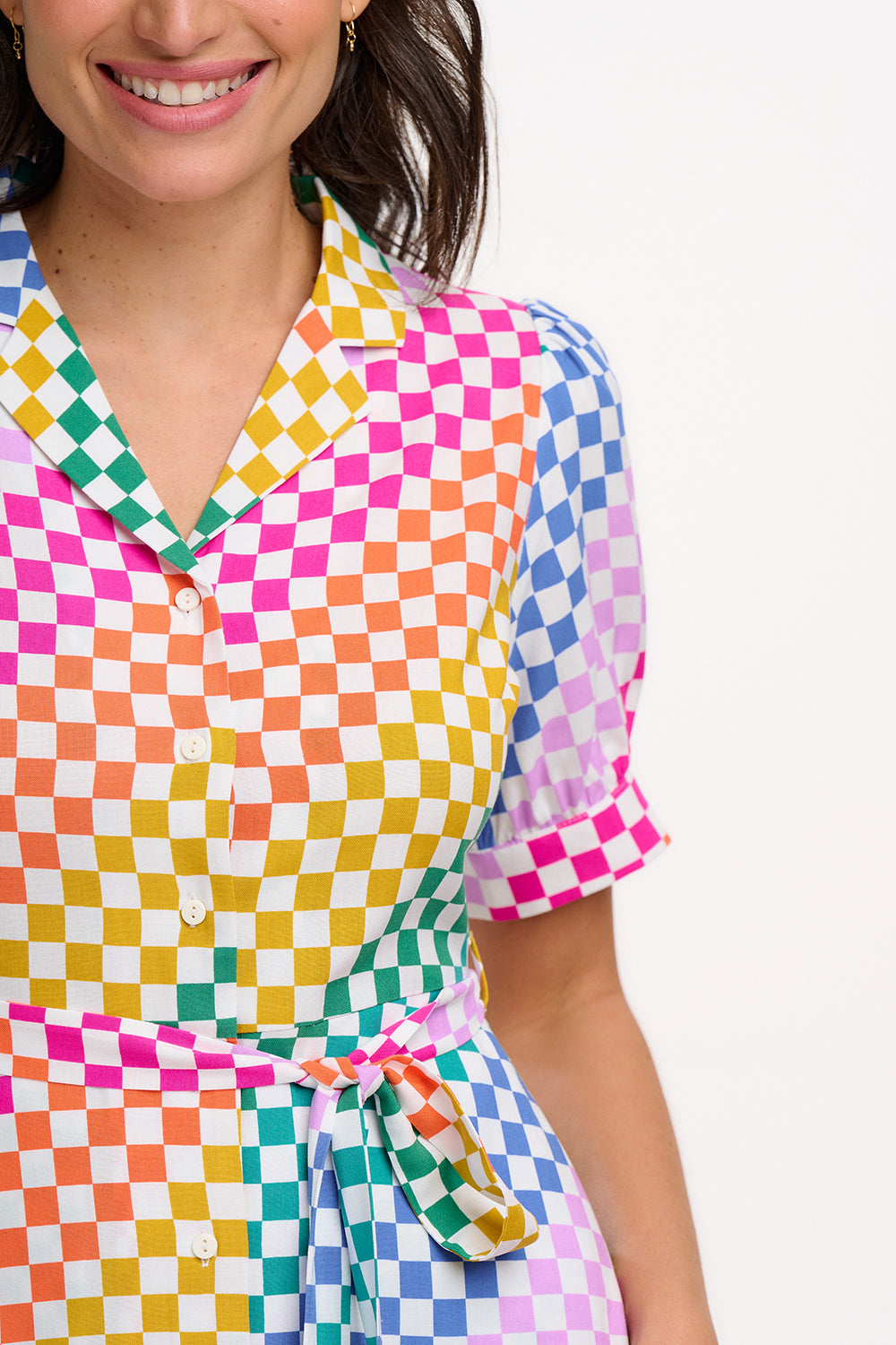 A model wearing a midi length shirt dress with a rainbow checkerboard pattern, featuring a lapel collar and puff sleeves.
