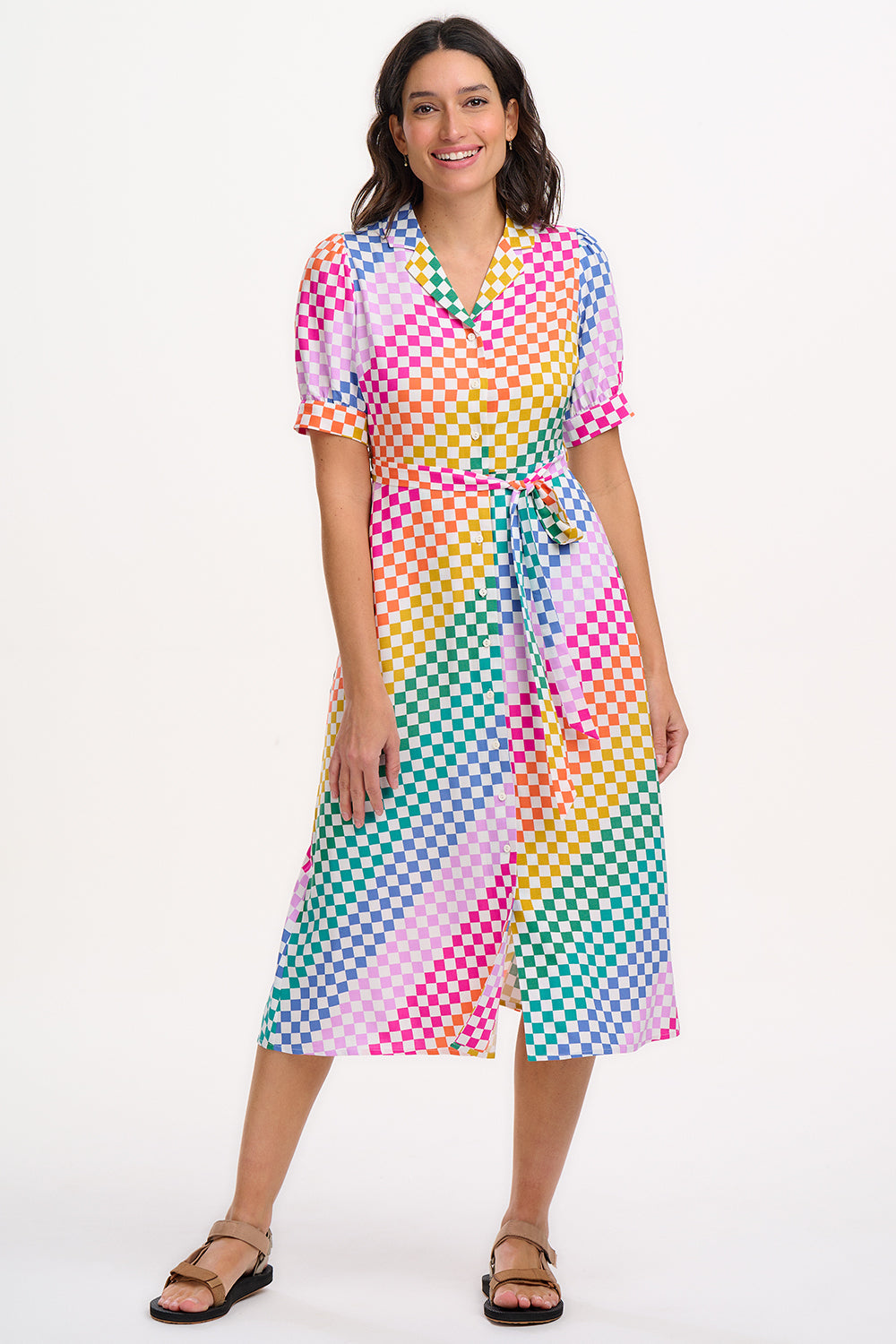 A model wearing a midi length shirt dress with a button placket and puff sleeves, featuring a multicolor rainbow checkerboard pattern.