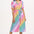 A model wearing a midi length shirt dress with a button placket and puff sleeves, featuring a multicolor rainbow checkerboard pattern.