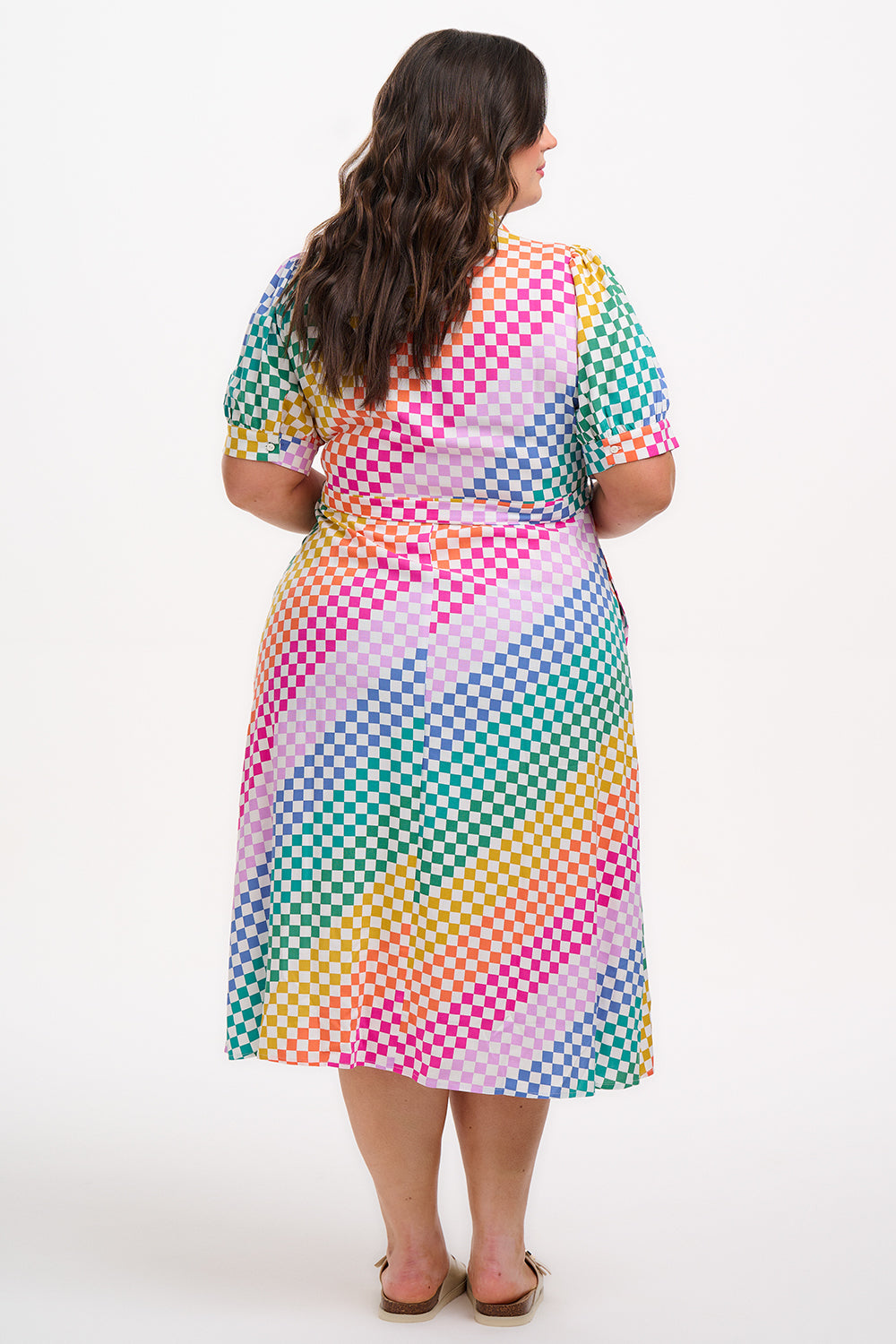 A model wearing a midi length shirt dress with a rainbow checkerboard pattern, featuring a lapel collar and puff sleeves.