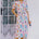 A model wearing an off-white midi-length shirt dress with a Jungle Tile print, featuring colorful tropical wildlife, fruit, and plants. The dress has a button placket, puff sleeves, and a tie waist.