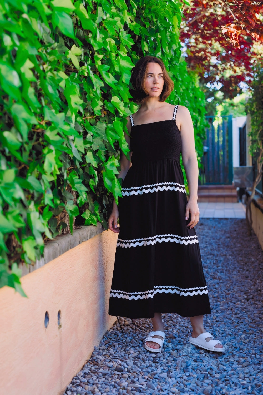 Woman in a black dress with white trim standing against a green wall.
