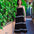 Woman in a black dress with white trim standing against a green wall.