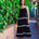 Woman in a black dress with white trim standing against a green wall.