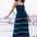 A model wearing a navy sundress with rainbow-colored Ric Rac embellishments on the hem and shoulder straps, standing by a railing.