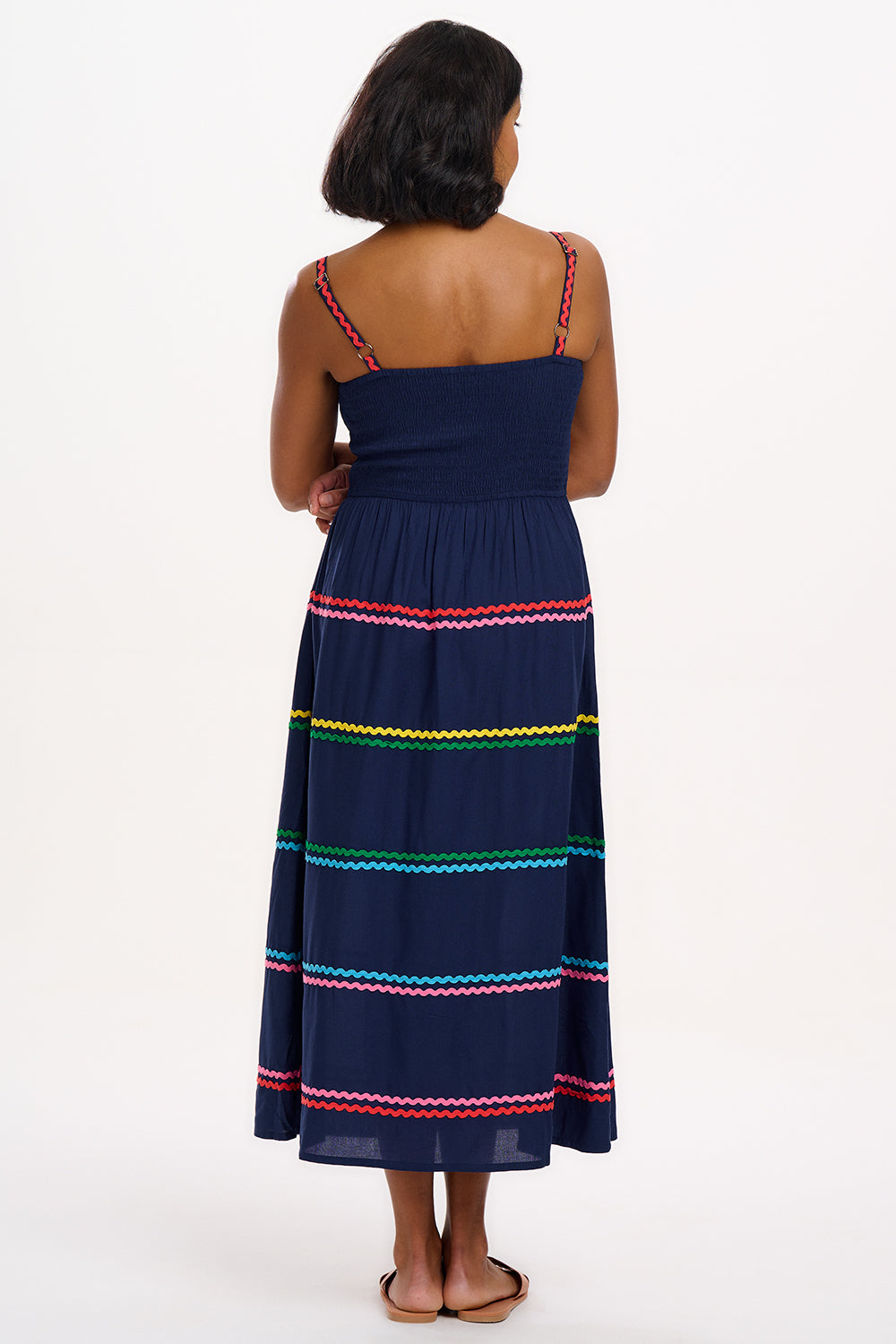 A model wearing a navy sundress with rainbow-colored Ric Rac embellishments on the hem and shoulder straps