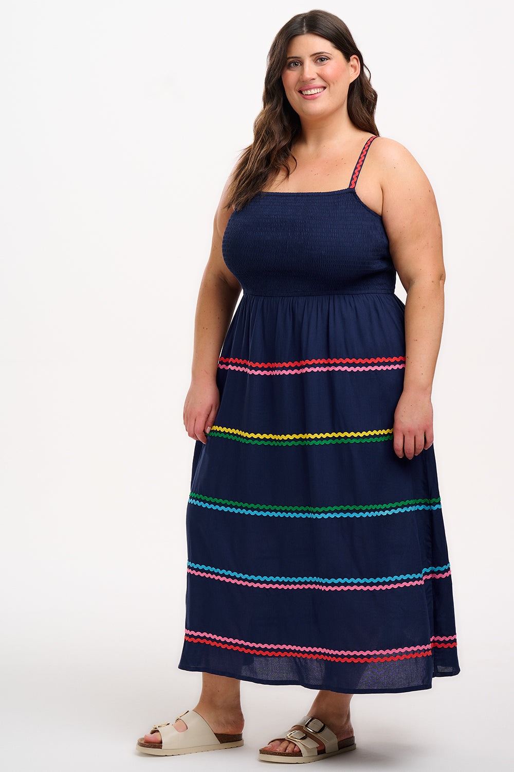 A model wearing a navy sundress with rainbow-colored Ric Rac embellishments on the hem and shoulder straps