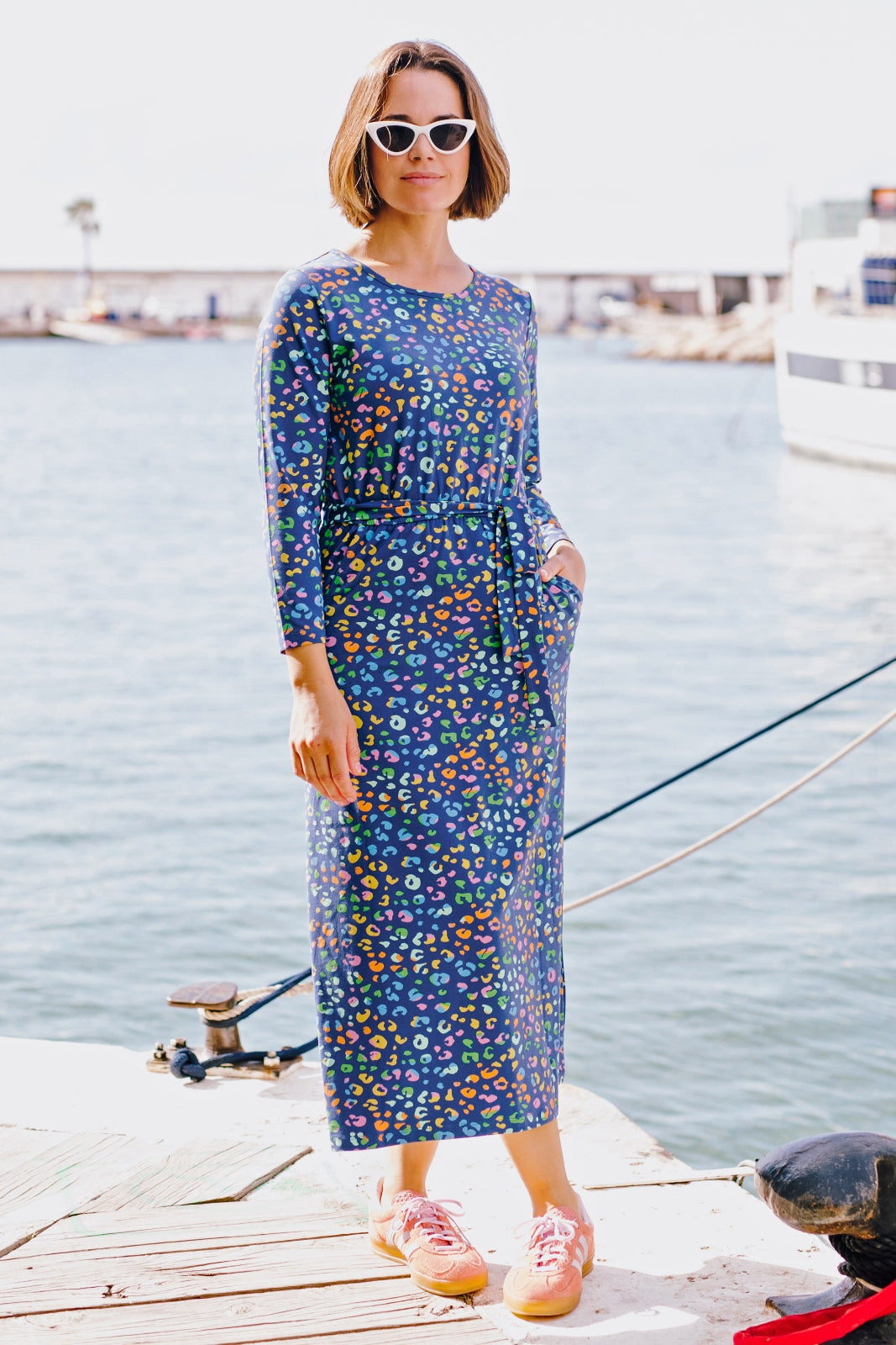 A model wearing a long sleeve midi jersey dress with a bright navy and mottled leopard print, paired with a matching tie belt, standing by a body of water.