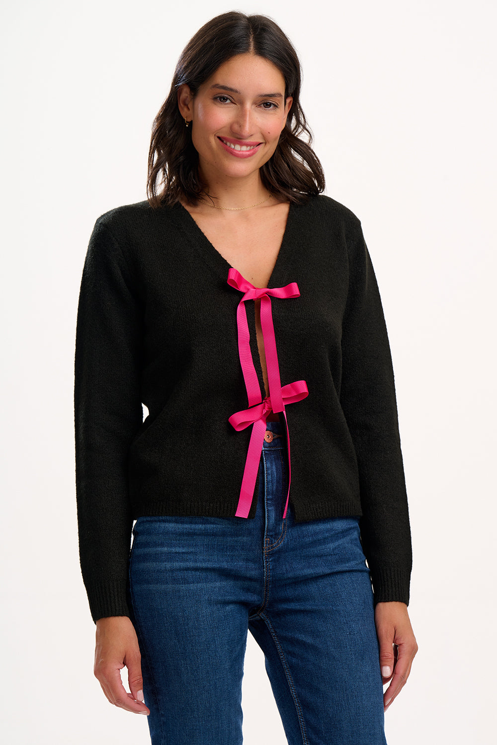 Woman wearing a black sweater with pink ribbons and blue jeans on a white background