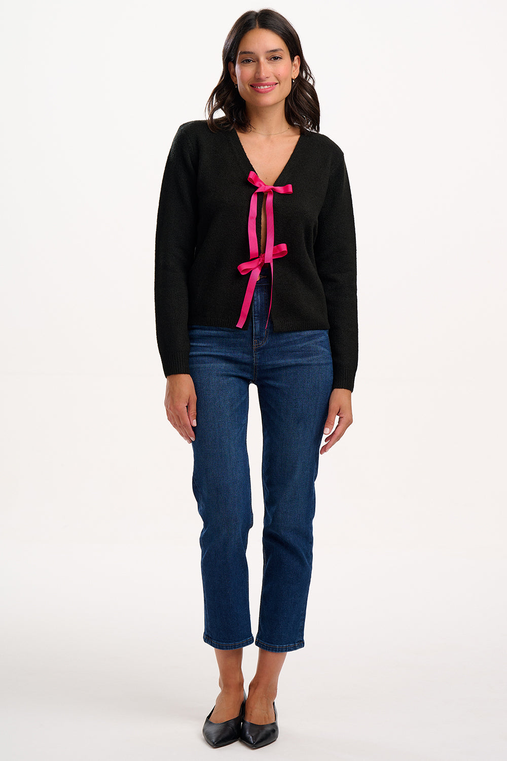 Woman wearing a black sweater with pink bows and blue jeans on a white background