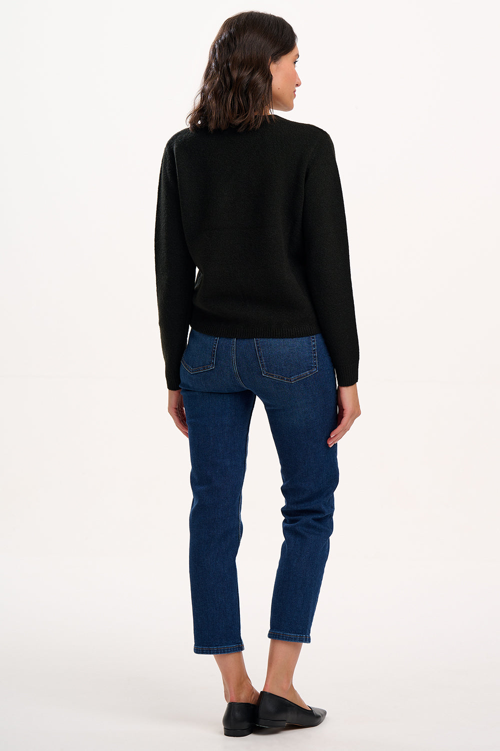 Woman wearing a black sweater and blue jeans on a white background