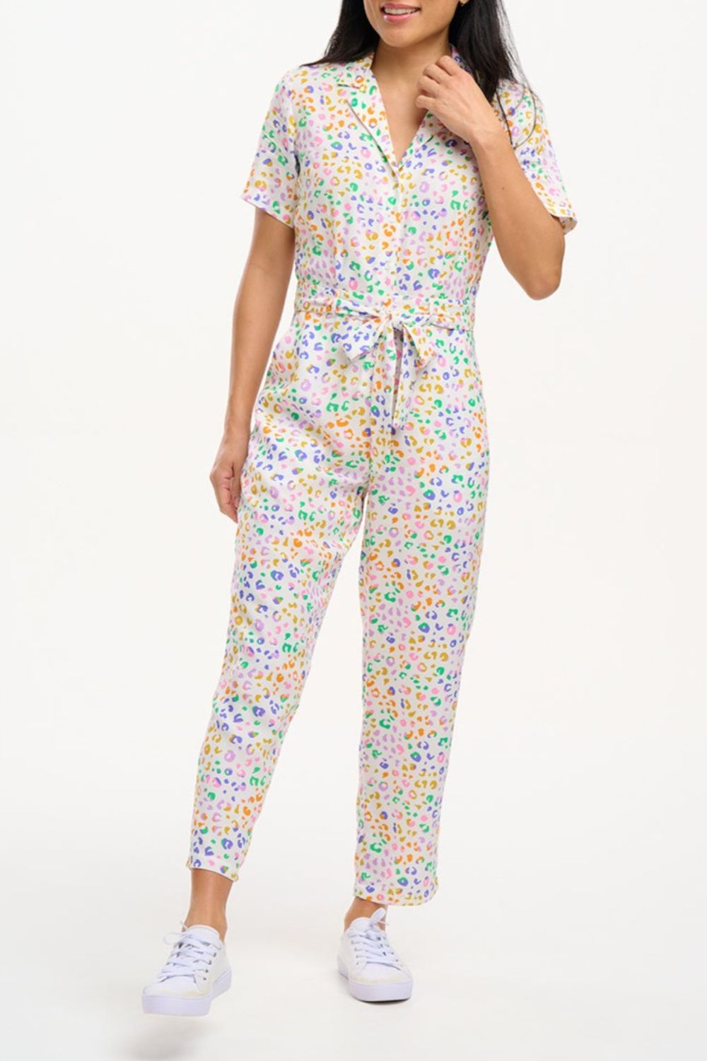 A model wearing an off-white jumpsuit with a mottled leopard print design, featuring short sleeves, a revere collar, side pockets, and a tie waist.