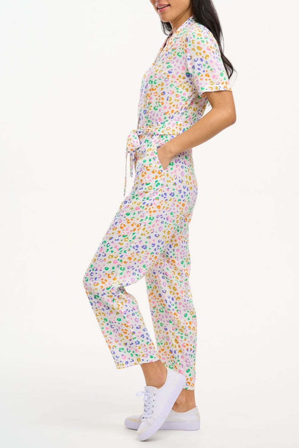 A model wearing an off-white jumpsuit with a mottled leopard print design, featuring short sleeves, a revere collar, side pockets, and a tie waist.