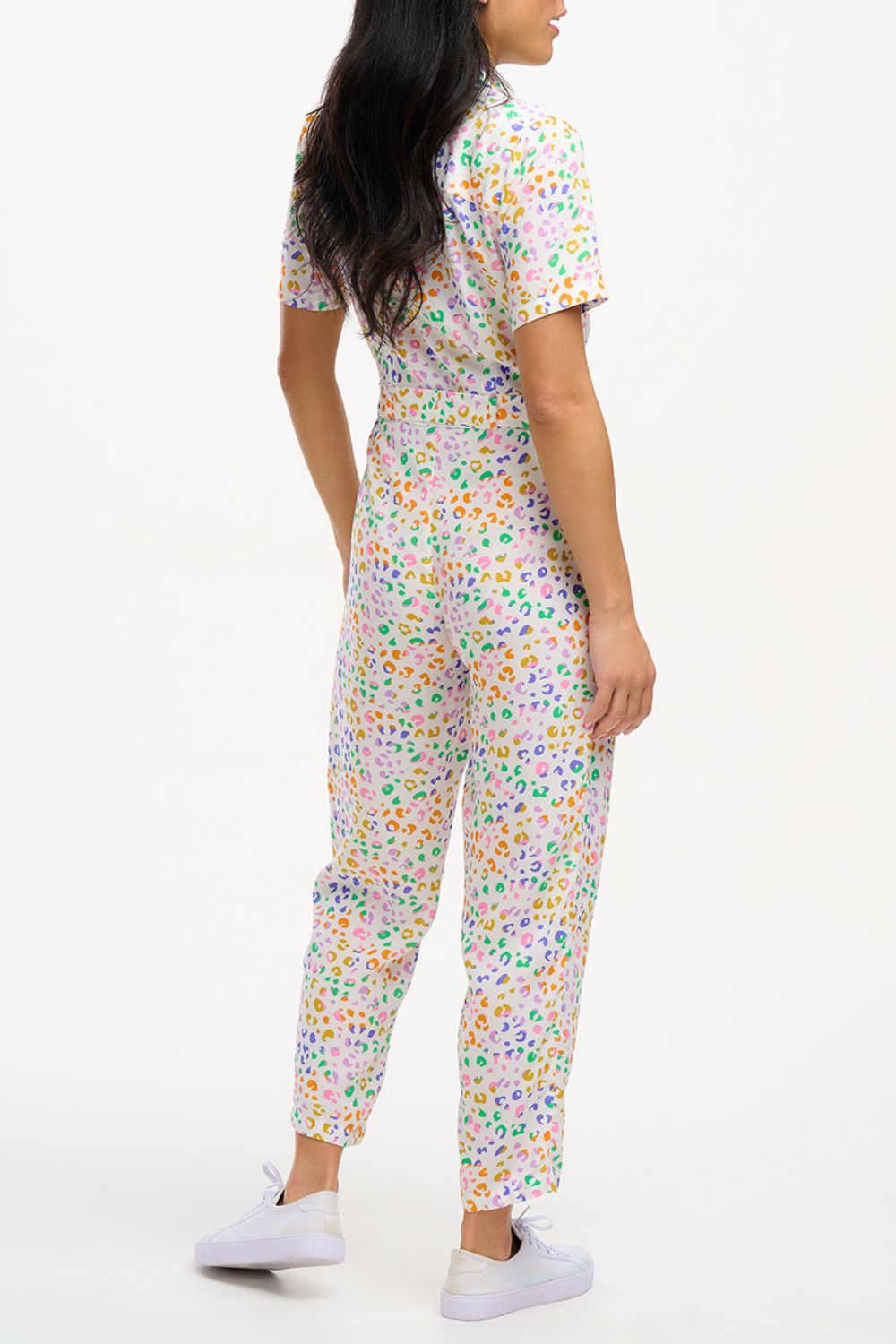 A model wearing an off-white jumpsuit with a mottled leopard print design, featuring short sleeves, a revere collar, side pockets, and a tie waist.