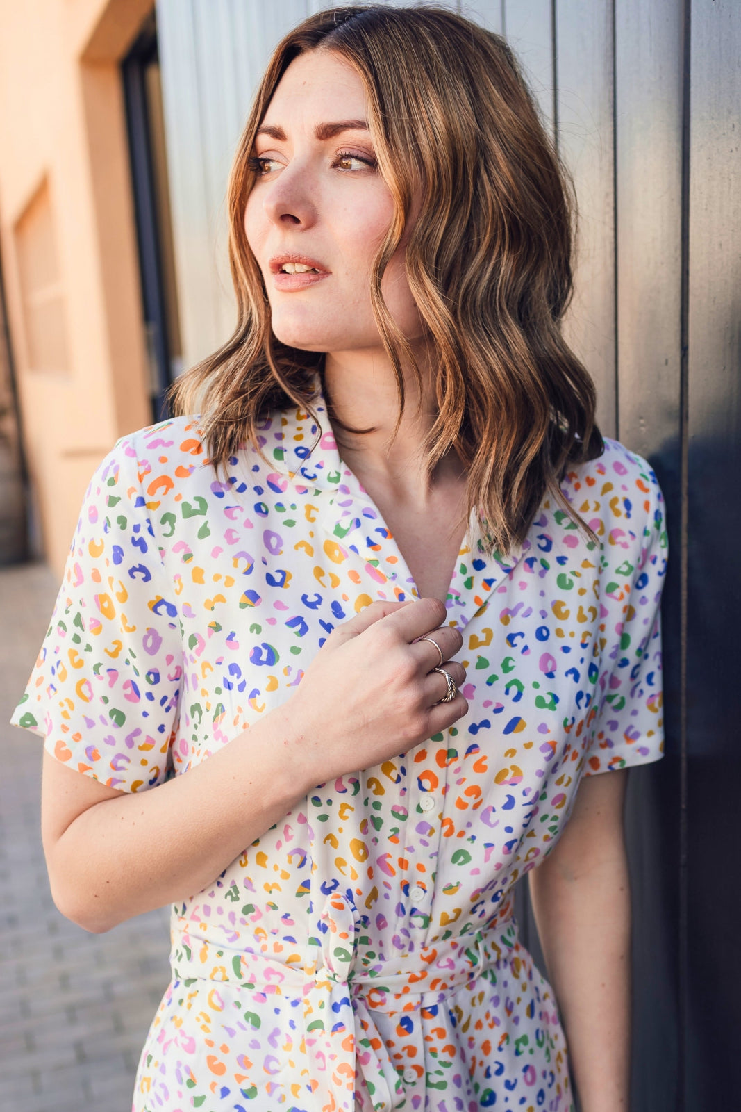 Woman wearing a colorful patterned shirt leaning against a wall.