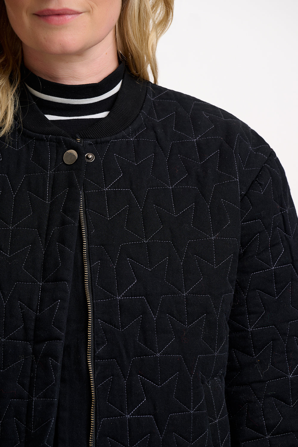 Close-up of a person wearing a black quilted jacket with geometric pattern on a white background