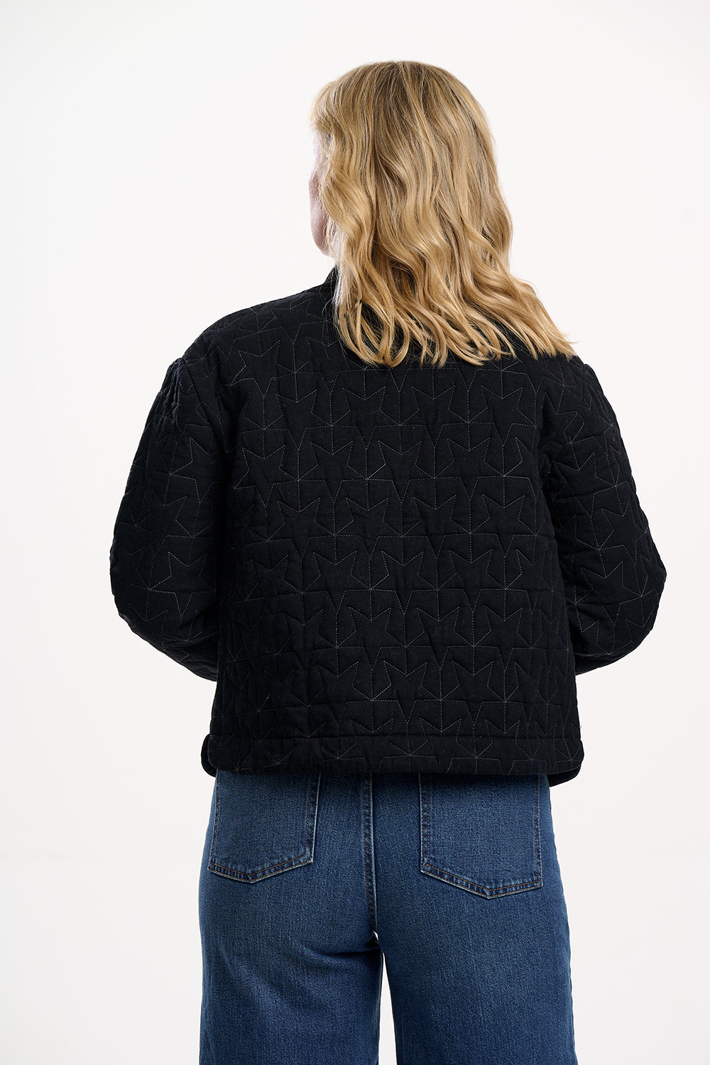 Person wearing a black quilted jacket and blue jeans on a white background
