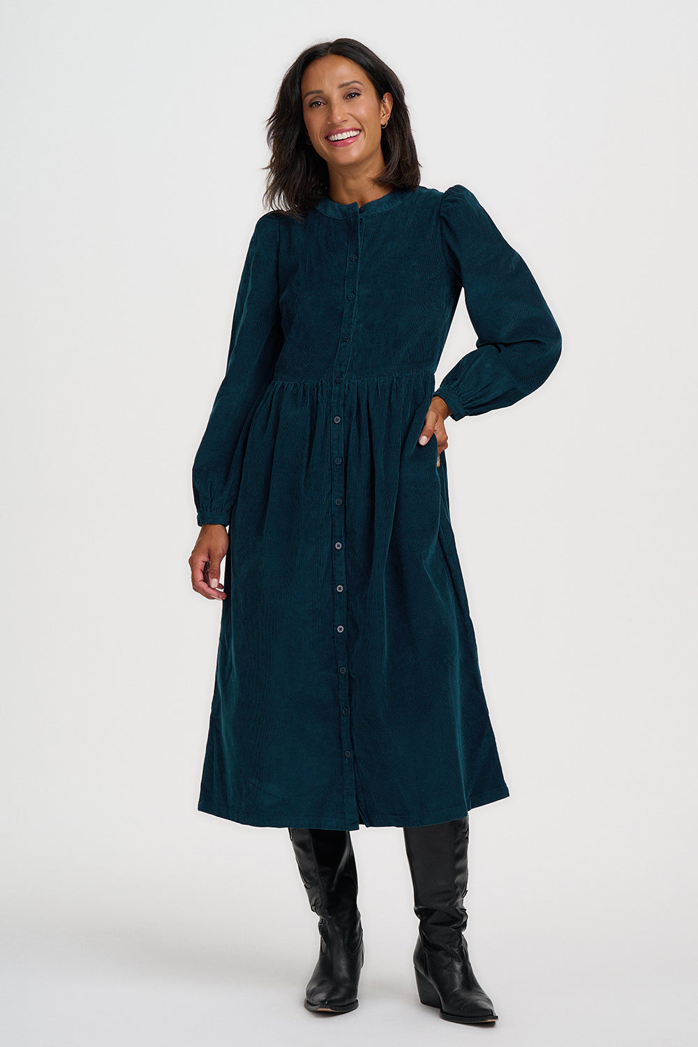 A woman modeling a long-sleeved navy blue midi dress with a button-down front, puff sleeves, and a gathered waist, paired with black knee-high boots against a light gray studio background.