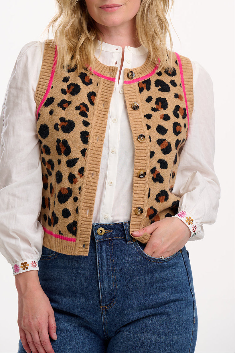 Woman wearing a leopard print cardigan with pink accents, white blouse, and blue jeans on a white background