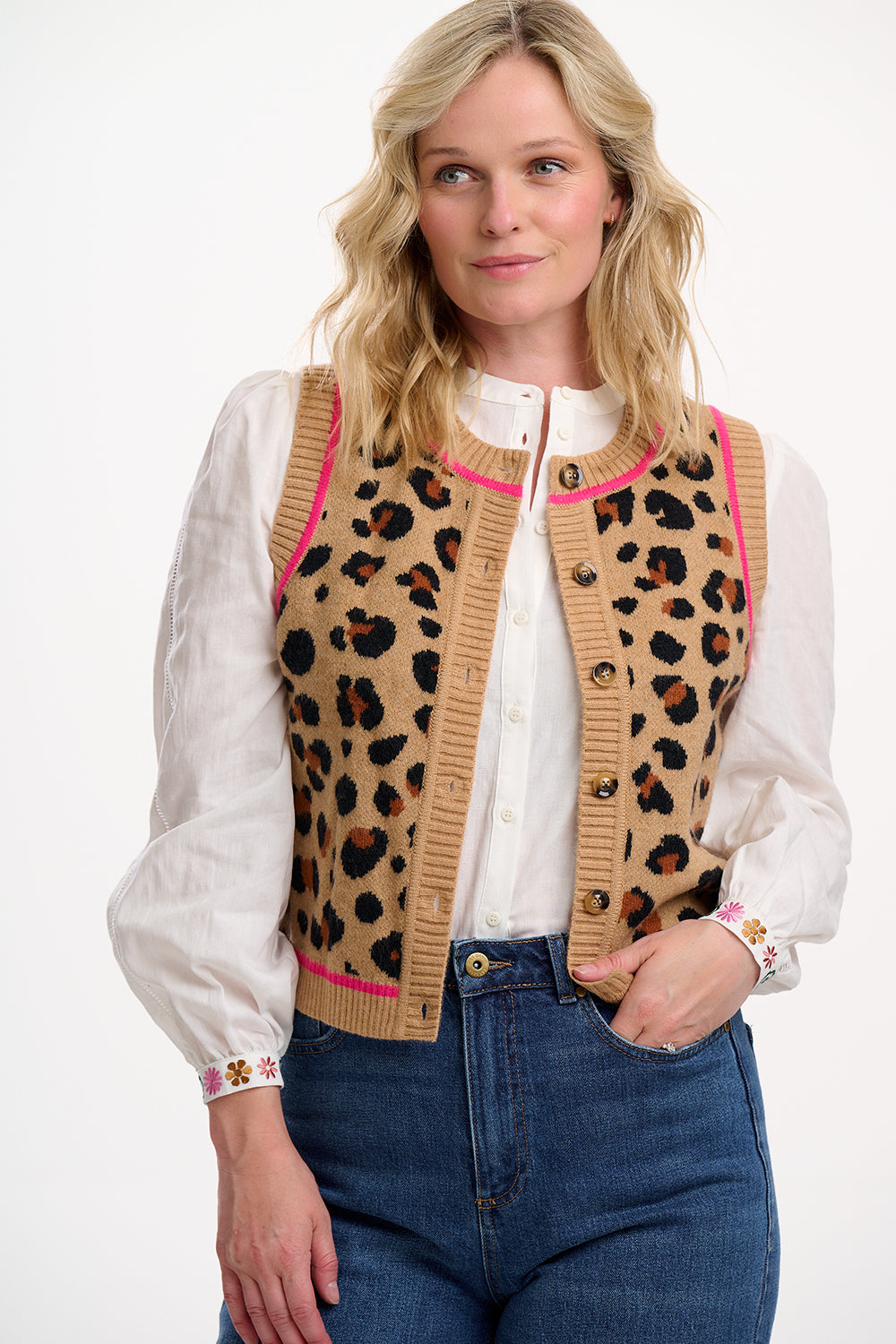 Woman wearing a leopard print cardigan with pink accents, white blouse, and blue jeans on a white background