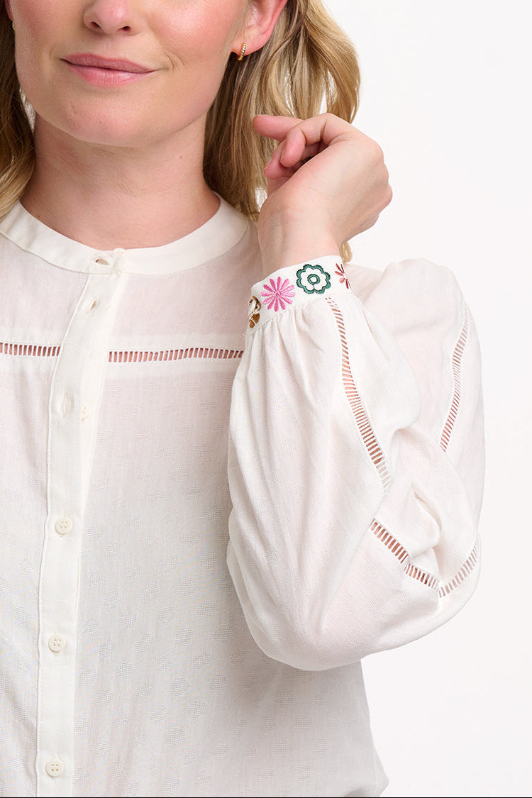 Woman wearing a white blouse with intricate designs on a plain background
