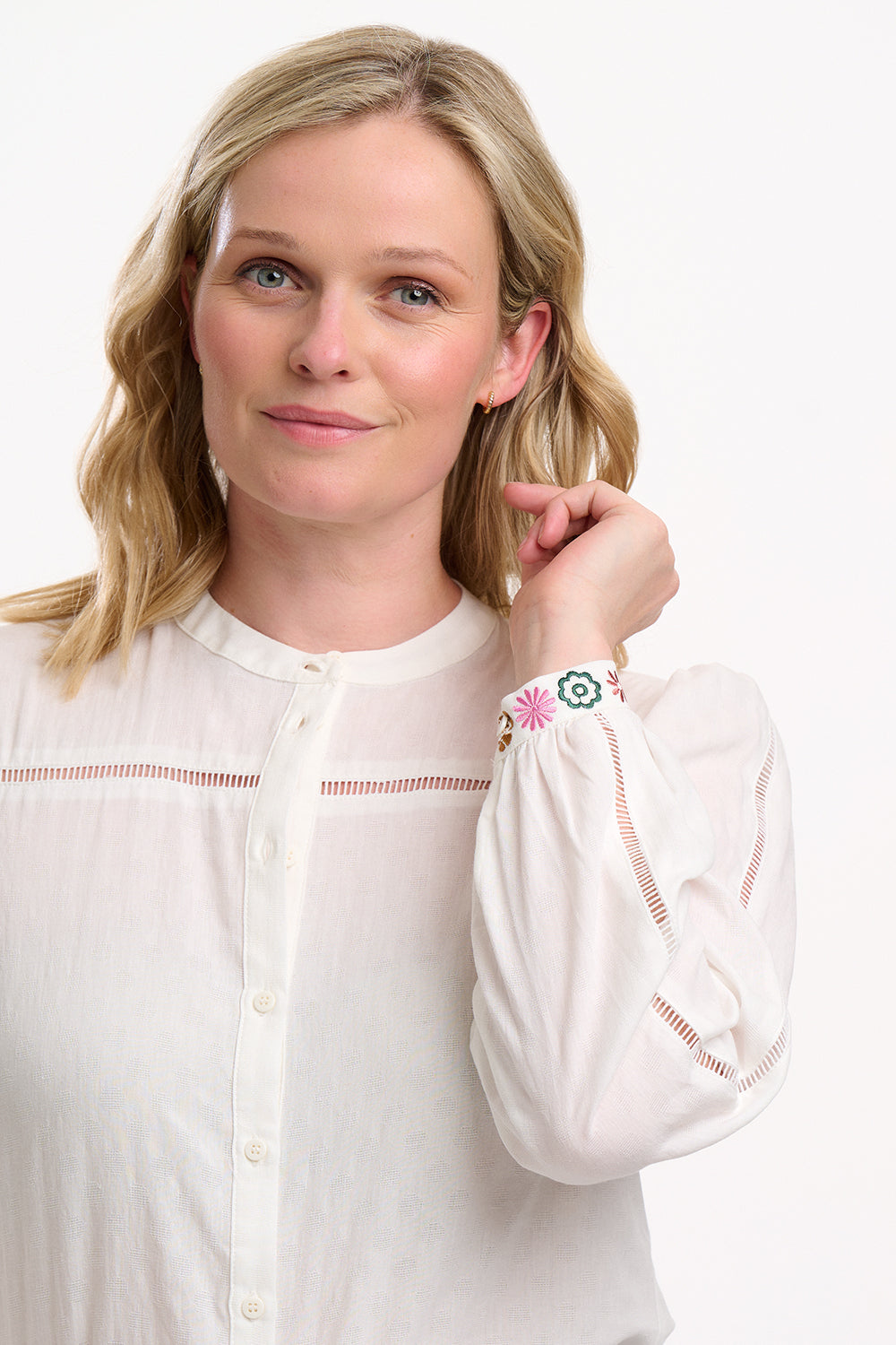 Woman wearing a white blouse with intricate designs on a plain background
