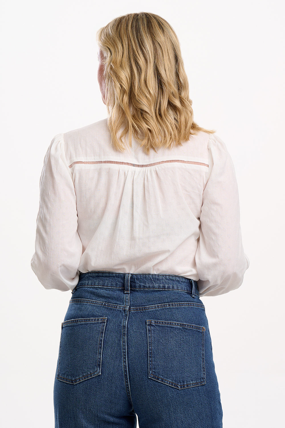 Person wearing a light-colored blouse and blue jeans on a white background