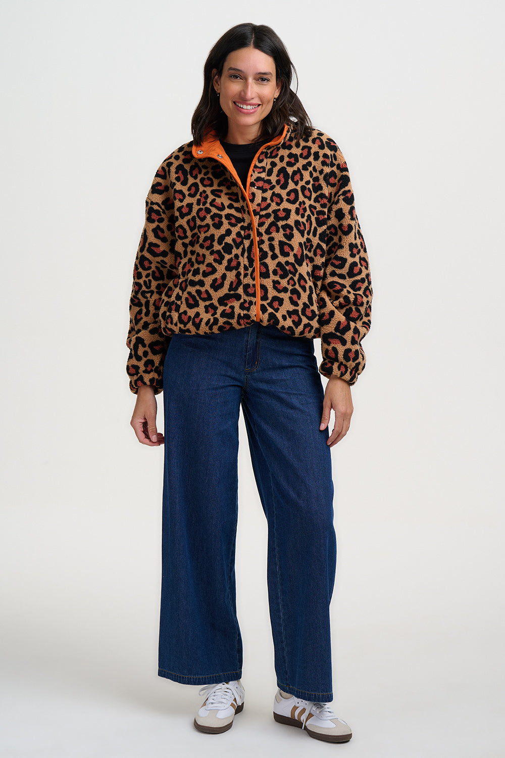 Woman wearing a leopard print jacket with orange zipper and blue jeans on a white background